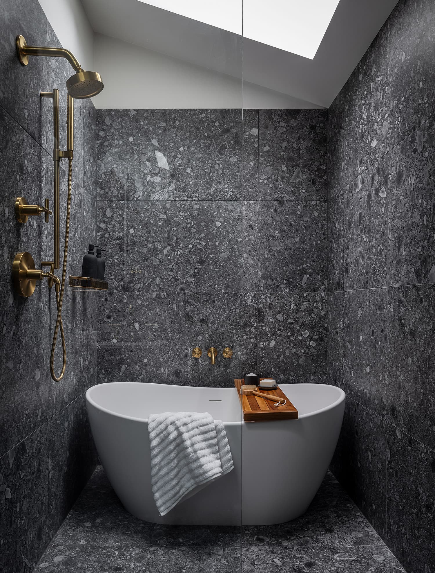 Stone master bath with freestanding soaker tub, skylight, and brass fixtures